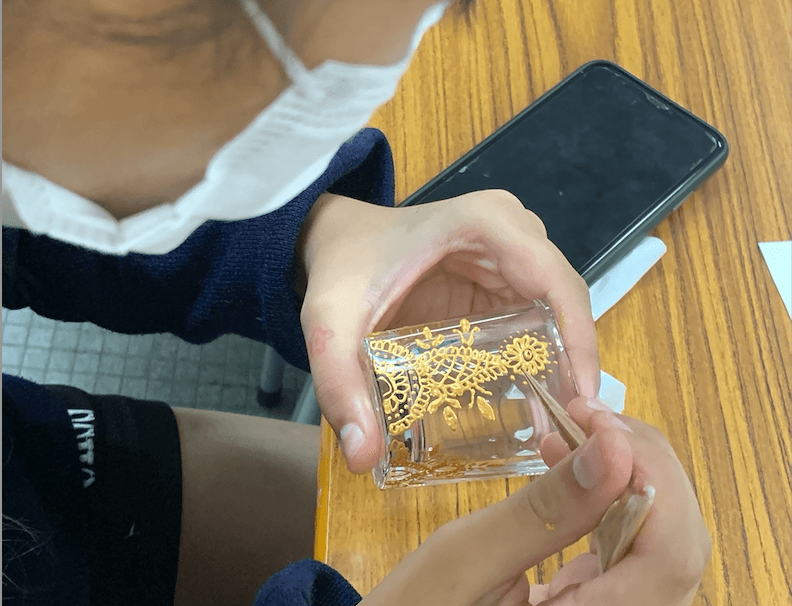 student drawing henna patterns on glass